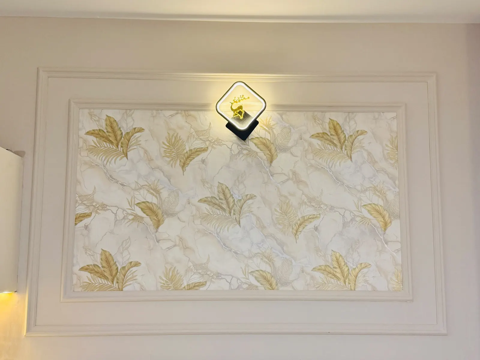Gold-leaf marble wallpaper panel framed in PU moulding with a sculptural wall light — homeZyard interior at Brigade Cornerstone Utopia, Varthur, Bengaluru